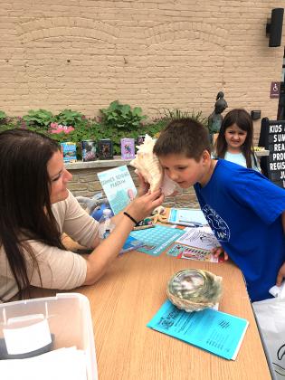 Stephanie Swenski (left) holds a conk shell for Jamison Shovald to hear the ocean during the Summer Reading Program kick-off on Tuesday, June 14. (submitted photo)