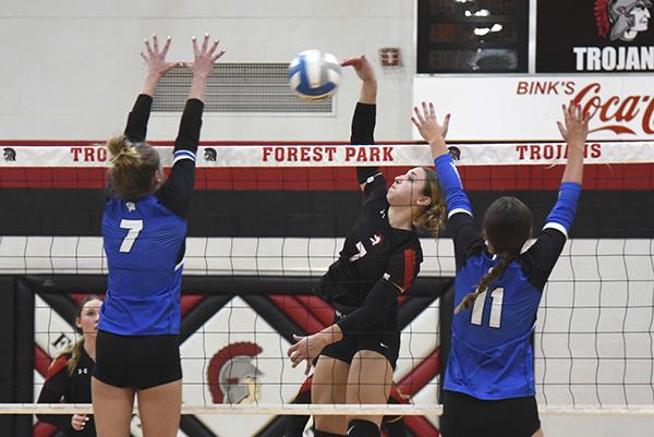 Trojan Ava Fischer #7 tipping the ball over the net, while Wykons Danica Shamion #7 and  Kya Dallavalle #11 attempting to block the ball.