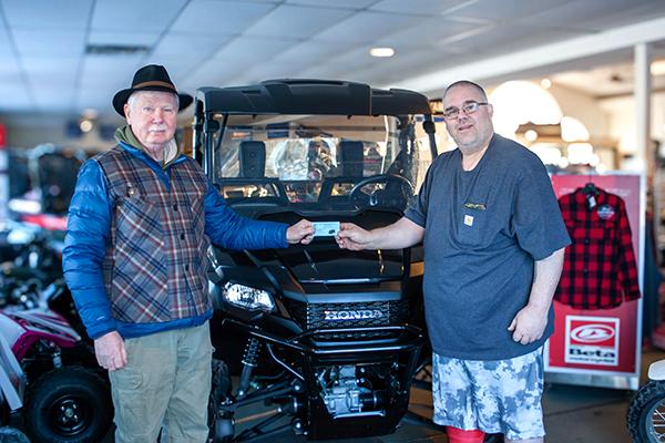 Pictured are, John Budde handing his winning ticket to STSC President Tony Erickson. They are standing in front of Mr. Buddes new 2023 Honda side by side.  (Submitted photo.)